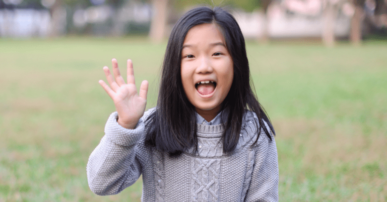 A child in a field waving hello to the camera.