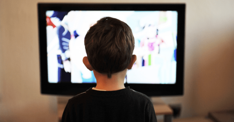 A child watching TV. The screen is blurred and is not completely visible as the child's head is in the way.