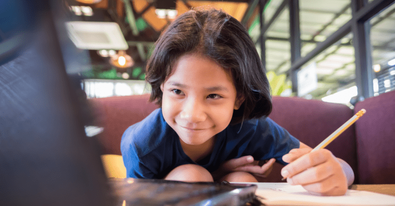 A child learning. He is using a pencil to take notes of what he is reading off of a computer.