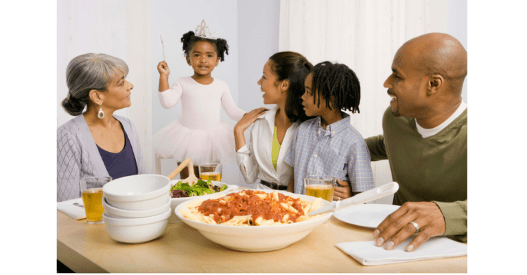 A young ballerina is dancing next to the table while her mom, dad, grandmother, and sibling watch her, indicating that the child might need to be taught how to stay at the table.